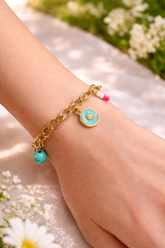 Gold chain charms bracelet on wrist with turquoise heart pendant and pink bead