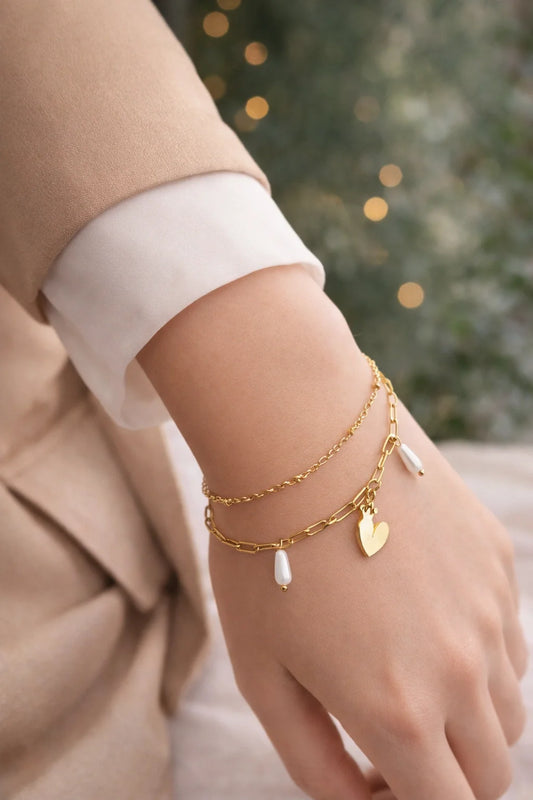 Gold-tone charm bracelet on wrist with heart charm and dangling pearl drops