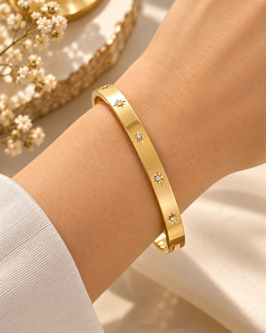 Gold kada bangle with small star-like gem accents, worn on wrist.