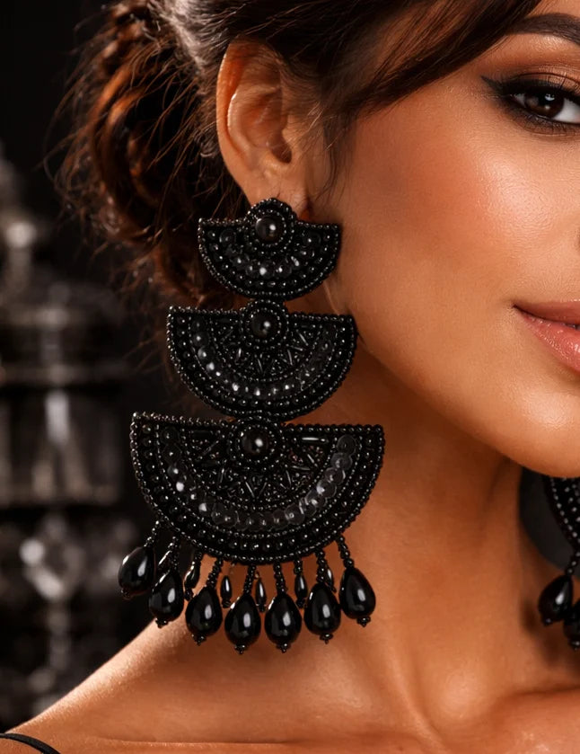Black long beaded earrings on ear, three stacked semicircle panels with teardrop fringe