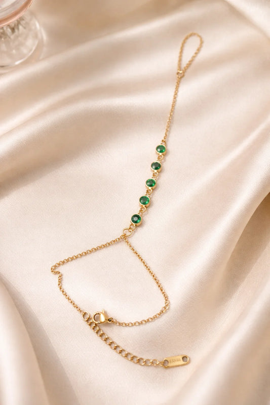 Gold-tone hand chain bracelet with green round stone links and small curved charm