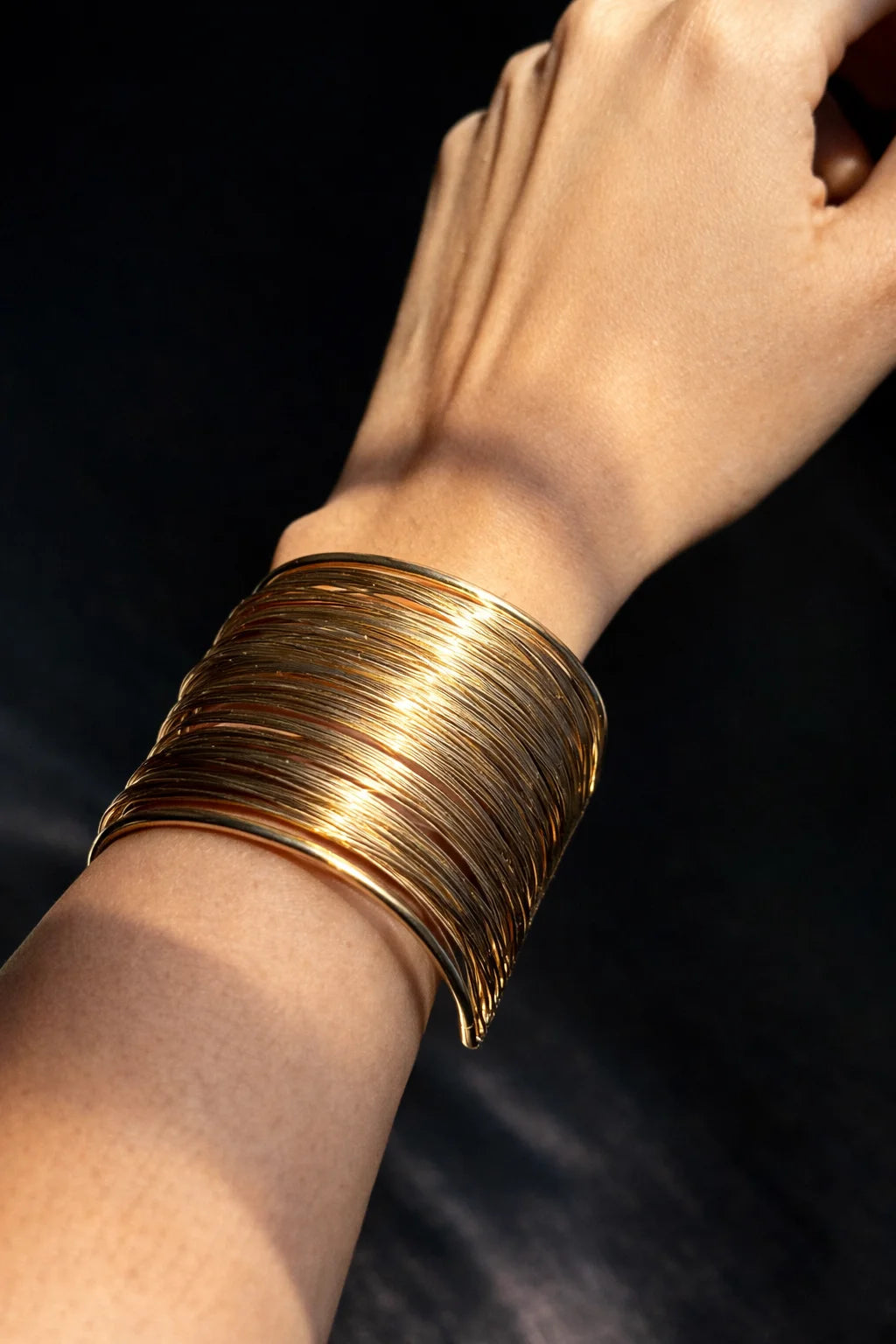 Gold-toned chunky bangle kada stacked on wrist with open cuff design
