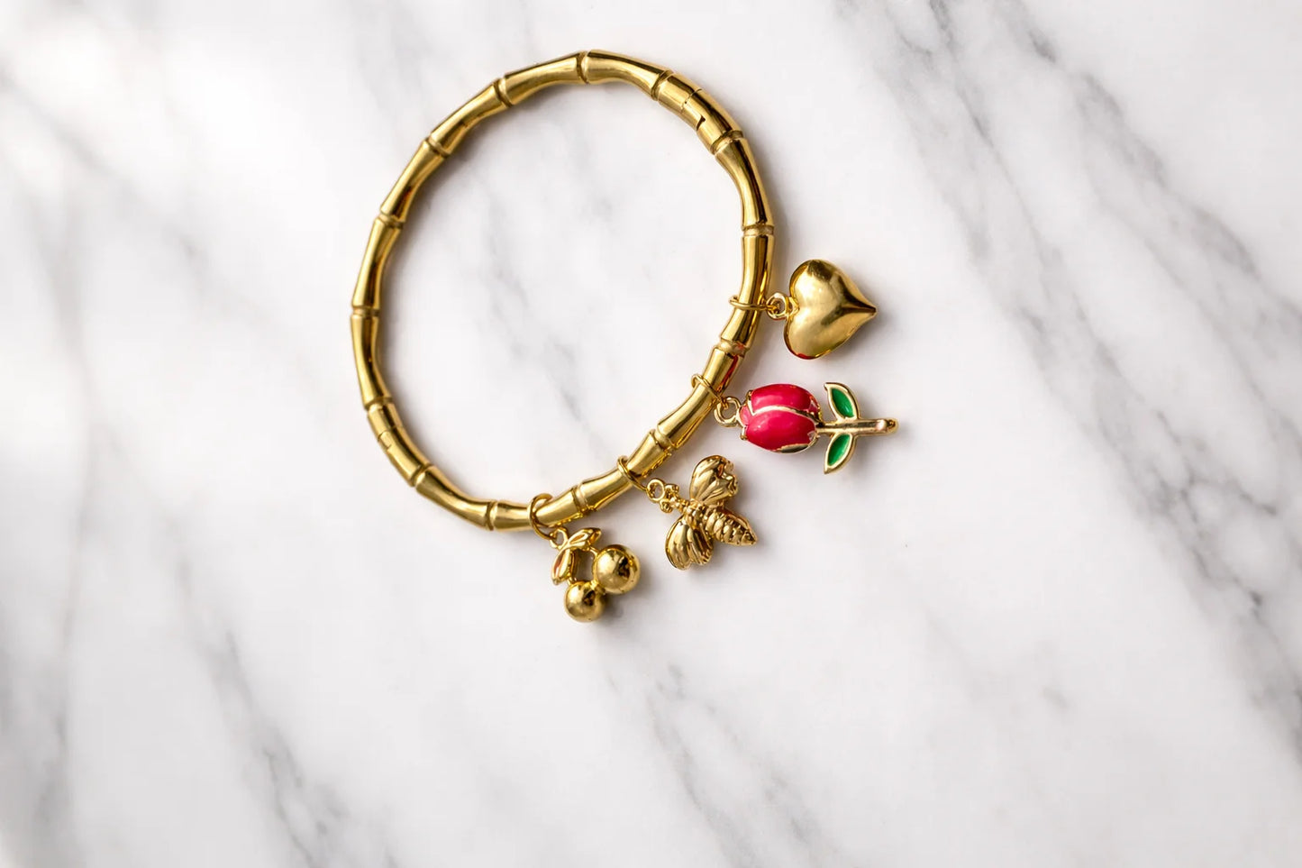 Gold bamboo kada bracelet with heart, tulip and red enamel rose charms on marble