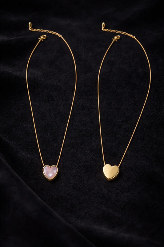 Gold heart necklace with two reversible pendants: pink and cream.