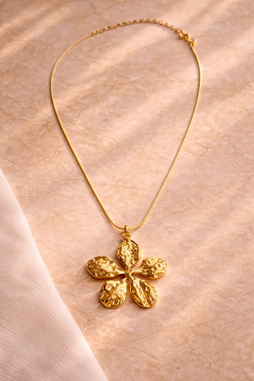 Gold-tone flower pendant necklace with textured five-petal charm and linked chain, full length