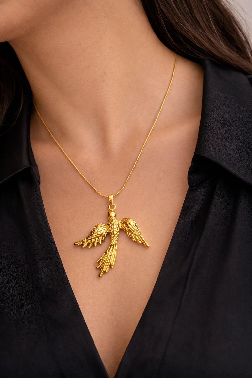Gold phoenix pendant necklace resting on a neckline, long chain with charm loop