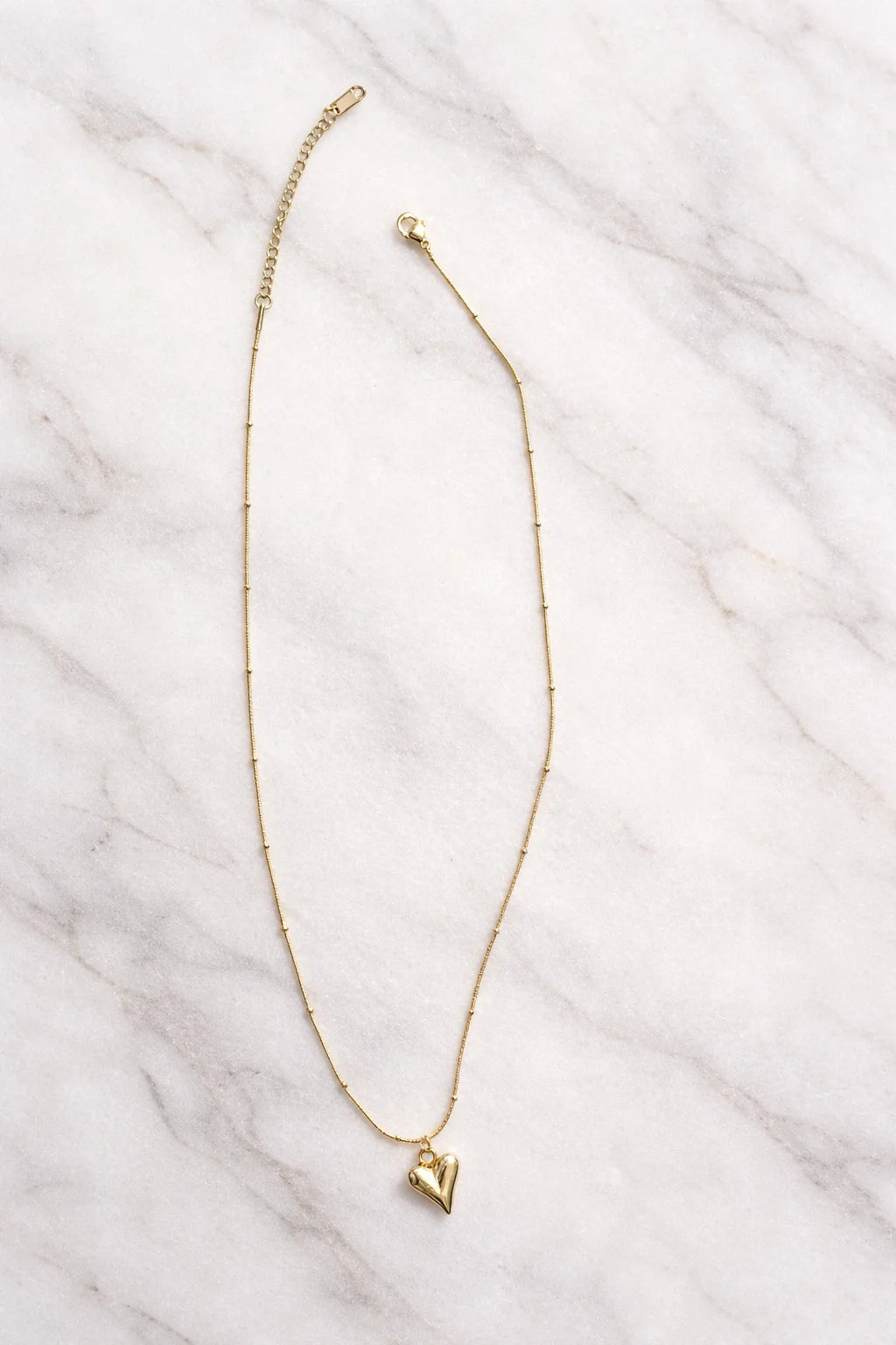 Gold heart pendant necklace with slim chain and small heart charm near the clasp
