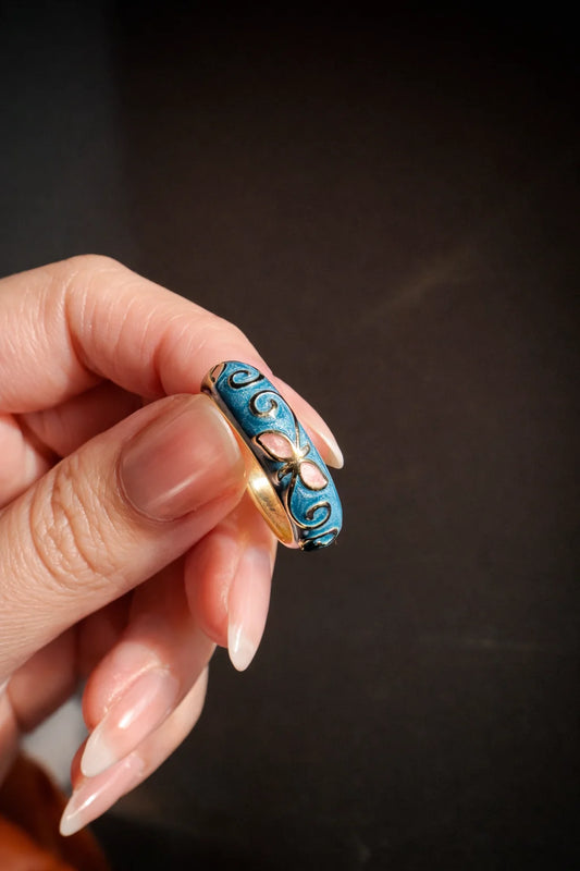 Blue enamel ring with gold edge, swirl details and pink insets on a slim band