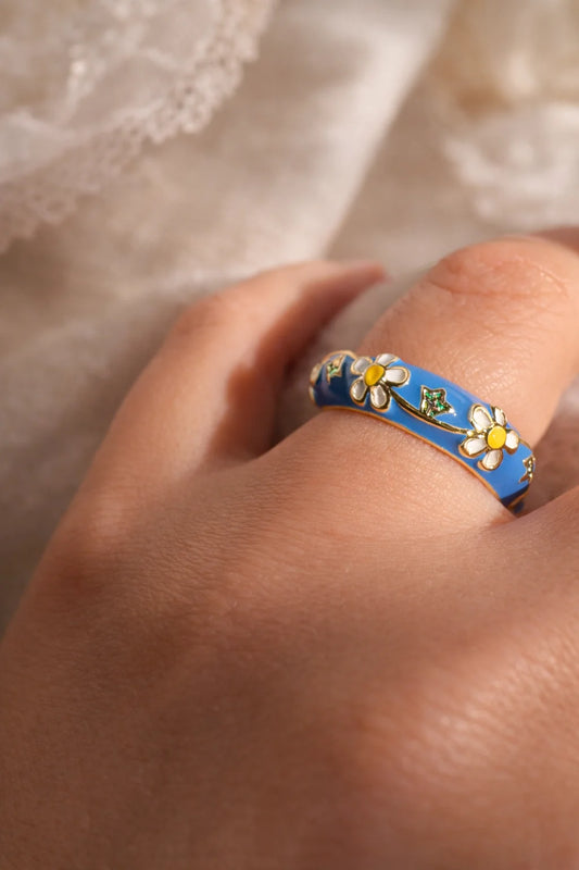 Enamel garden ring on finger, blue band with daisies and small leaf charms