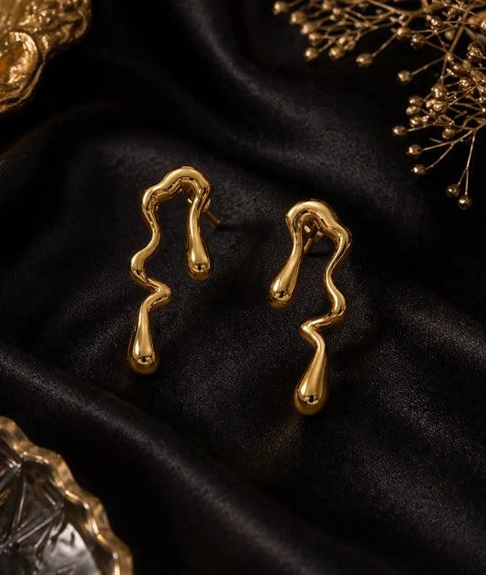 Gold-tone wavy teardrop dangle earrings, pair on dark satin fabric