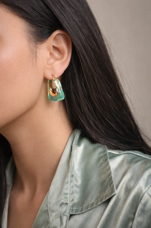 Gold-tone hoop earrings with green glass-like teardrop charms, worn