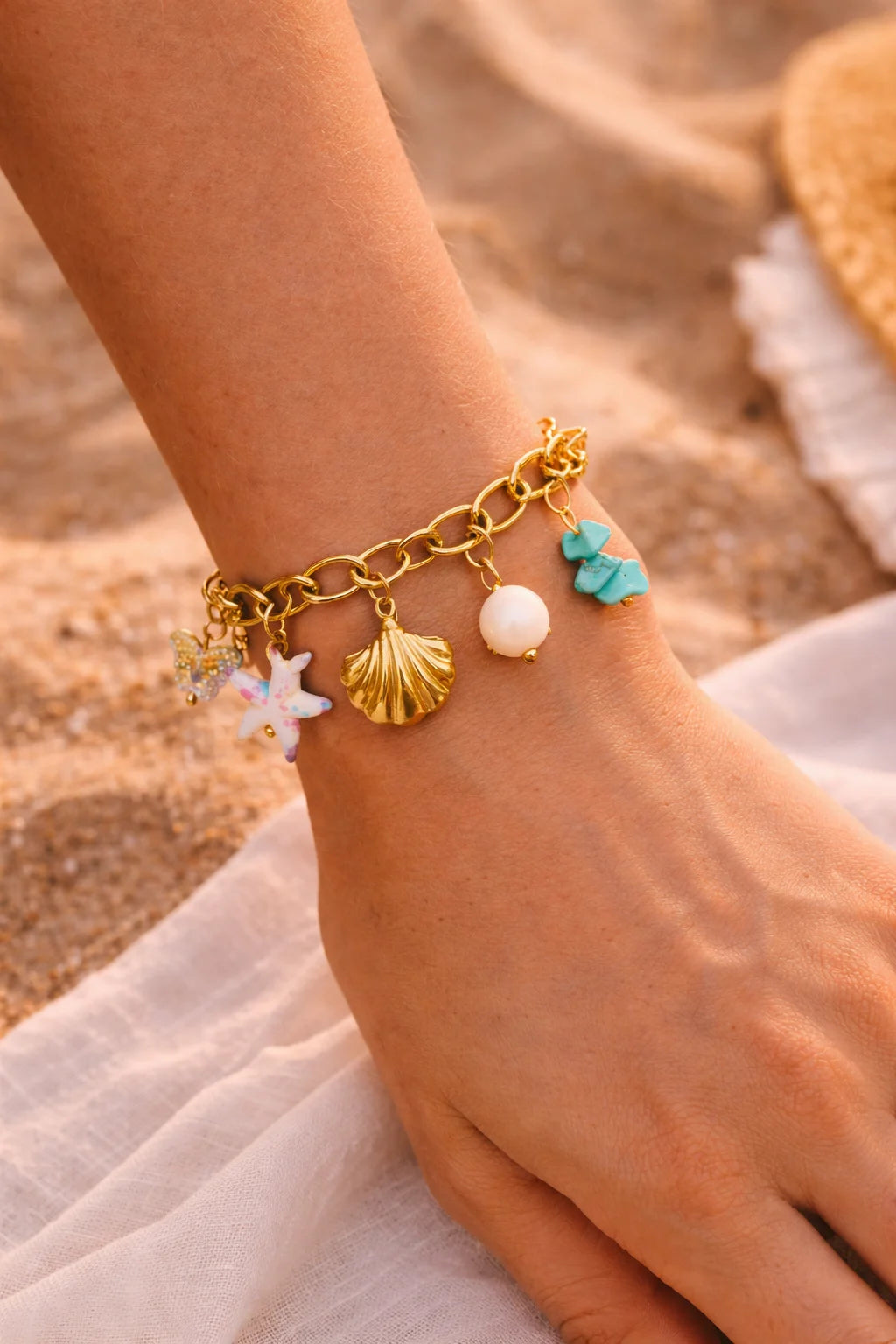 Gold-tone charm bracelet on wrist with starfish, seashell, pearl bead, and teal charm