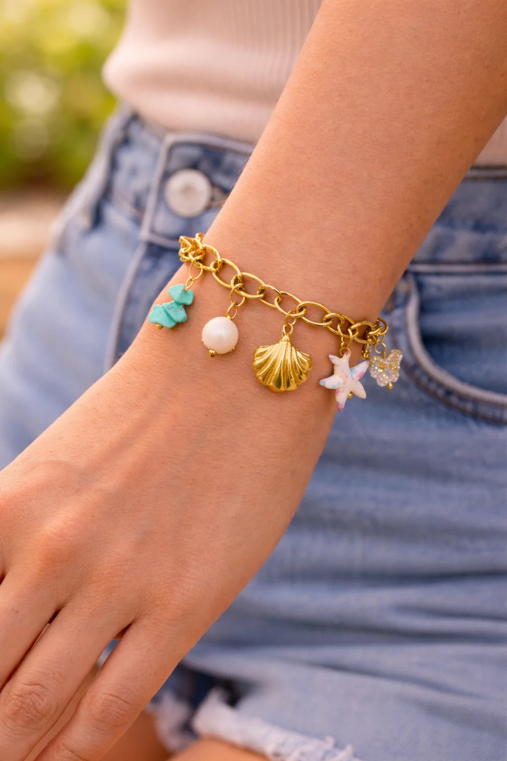 Gold-tone charm bracelet on wrist with seashell charm and two starfish plus pearl and teal