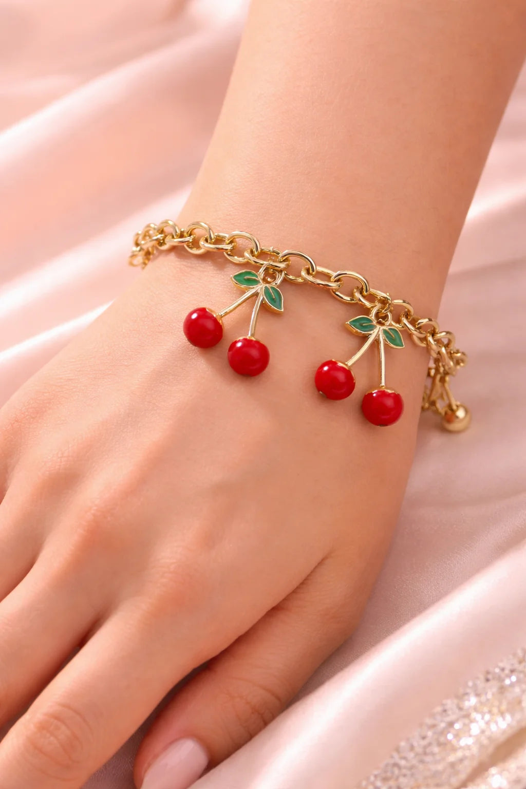Gold chain bracelet with dangling red cherries and green leaf charms