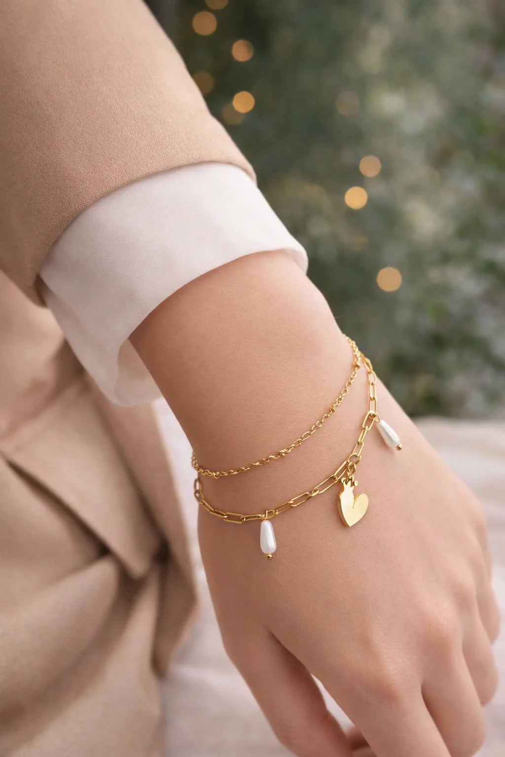 Gold-tone charm bracelet on wrist with heart charm and dangling pearl drops