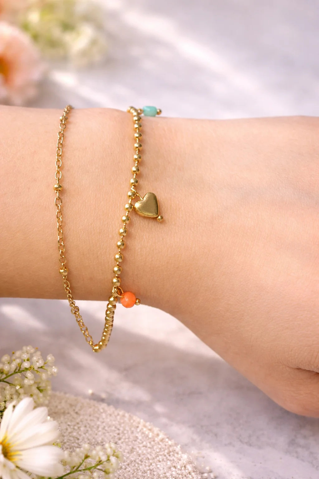 Layered gold heart charm bracelets on wrist with teal and orange bead accents