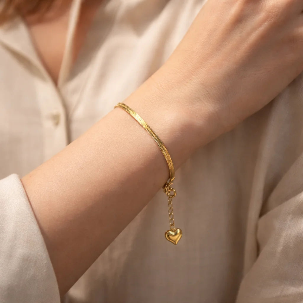 Gold-tone snake bracelet on wrist with heart drop charm and link chain