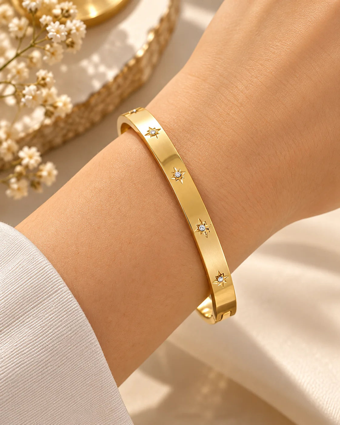 Gold kada bangle with small star-like gem accents, worn on wrist.