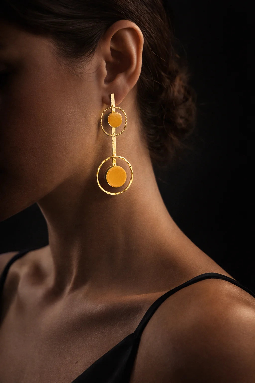 Gold-tone drop earrings on ear with orange round stones and halo ring details