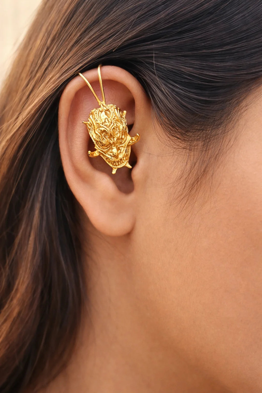 Gold-tone demon face ear cuff on ear, sculpted devil face detail