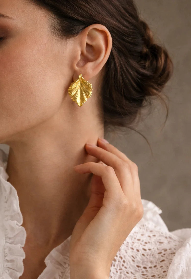 Gold-tone leaf drop earrings on ear, textured leaf design