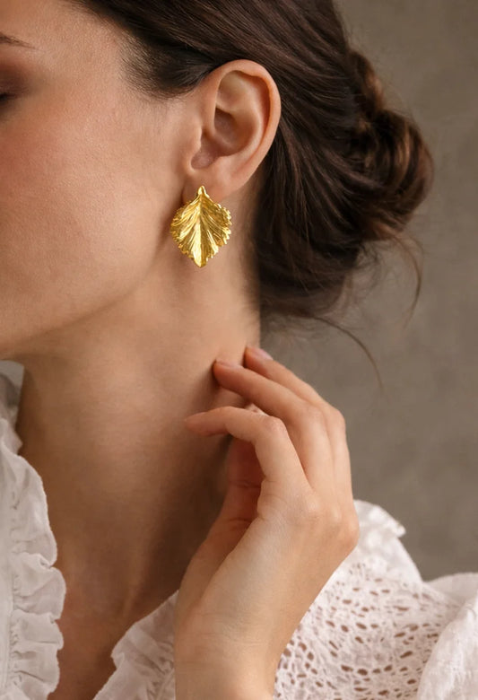Gold-tone leaf drop earrings on ear, textured leaf design