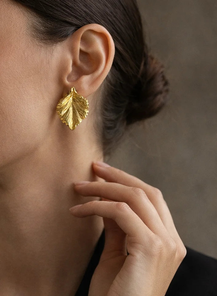 Gold-tone leaf drop earrings on ear, ribbed textured leaf details