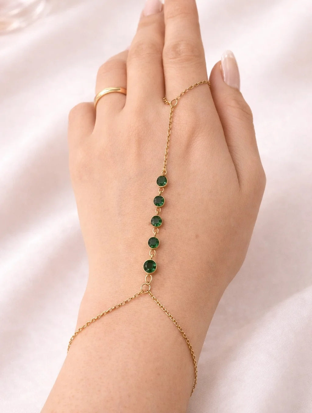 Gold-tone hand chain worn on hand with round green stones and bracelet links