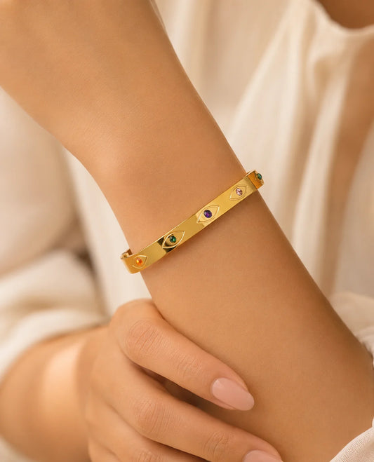 Gold-tone bracelet on wrist with small multicolor eye stones and hinged fit