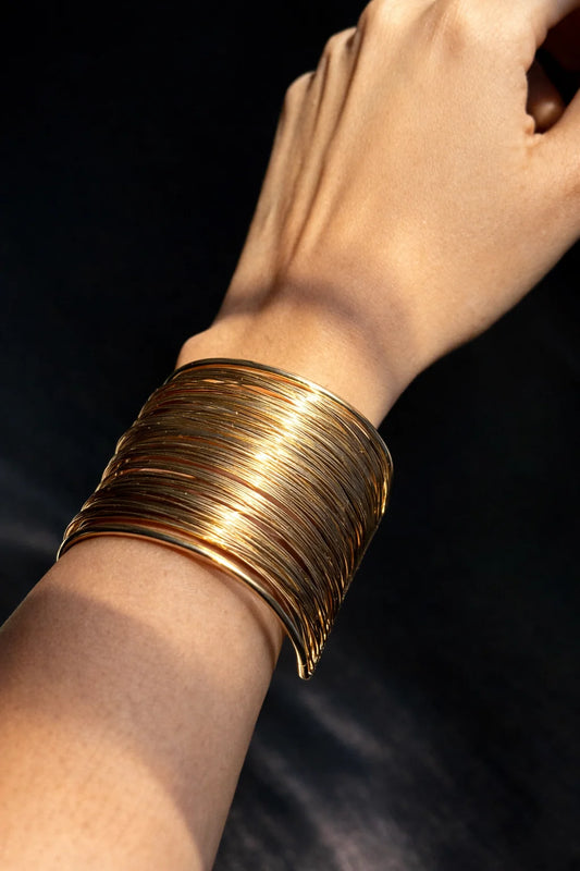 Gold-toned chunky bangle kada stacked on wrist with open cuff design