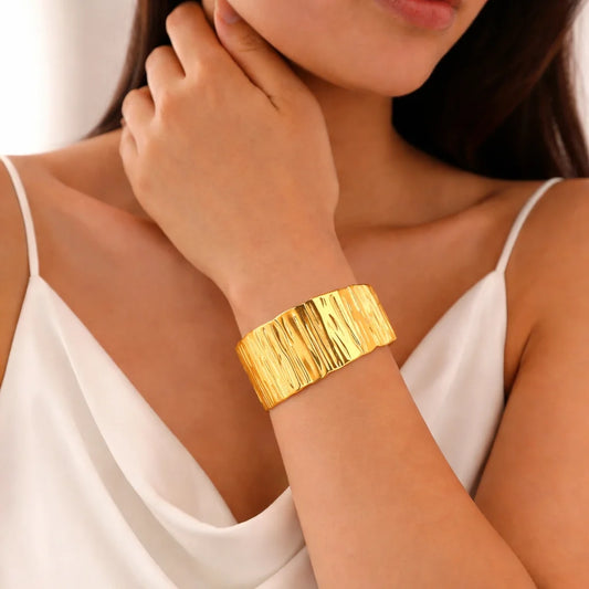 Gold wide cuff kada with vertical ripple pattern, worn on wrist over white dress