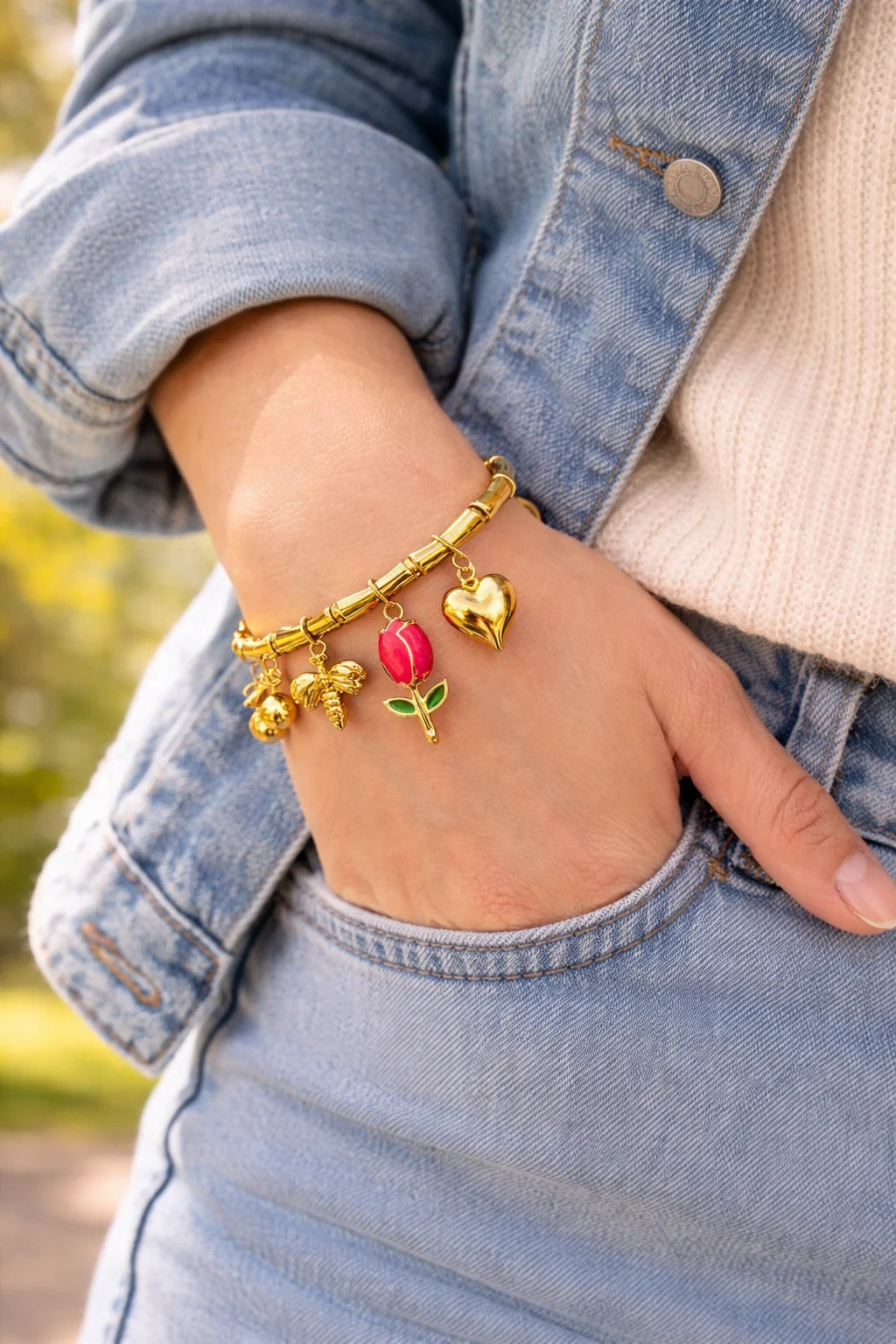 Gold kada bracelet on wrist with red tulip, heart and small flower charms
