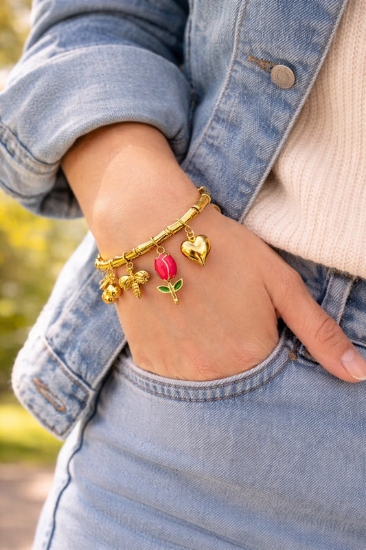 Gold charm bracelet on denim sleeve with heart and tulip red enamel charms