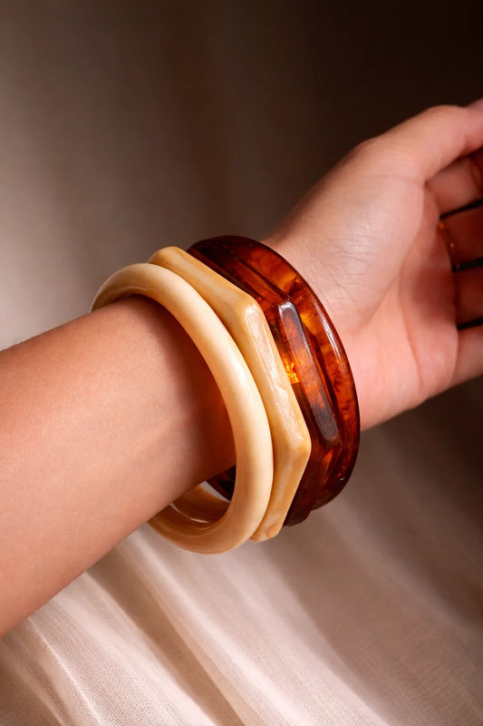 Resin bangles on wrist: cream and dark amber tortoise, rounded glossy cuffs