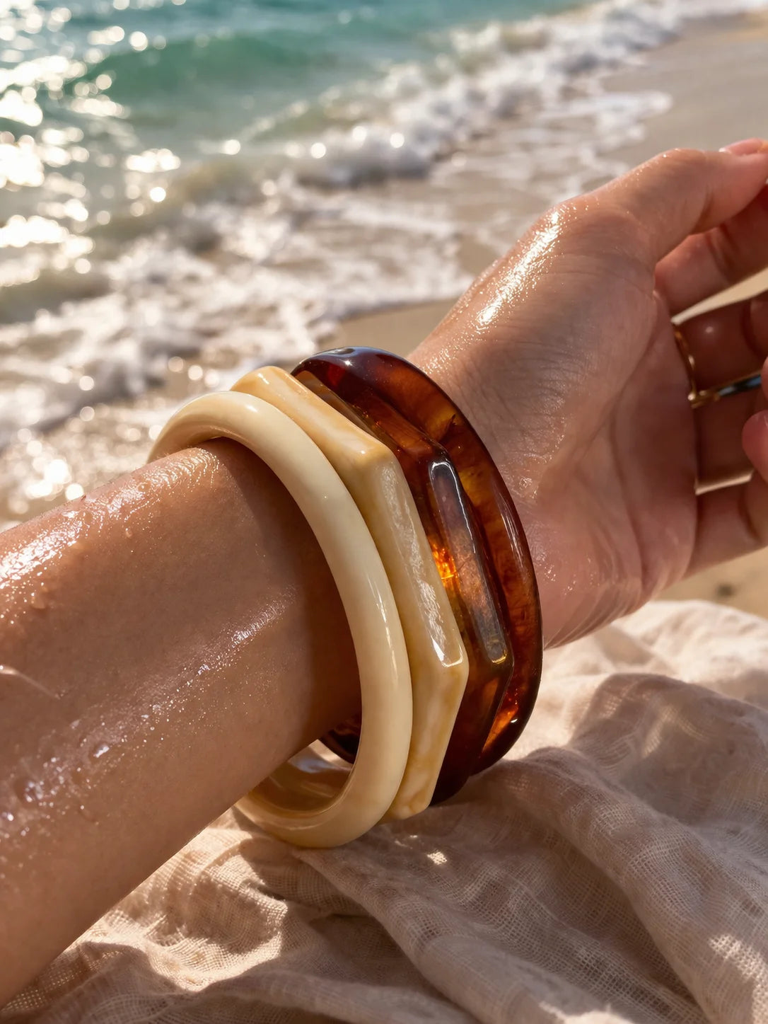 Stacked cream and dark amber resin bangles on wrist with glossy tortoiseshell band