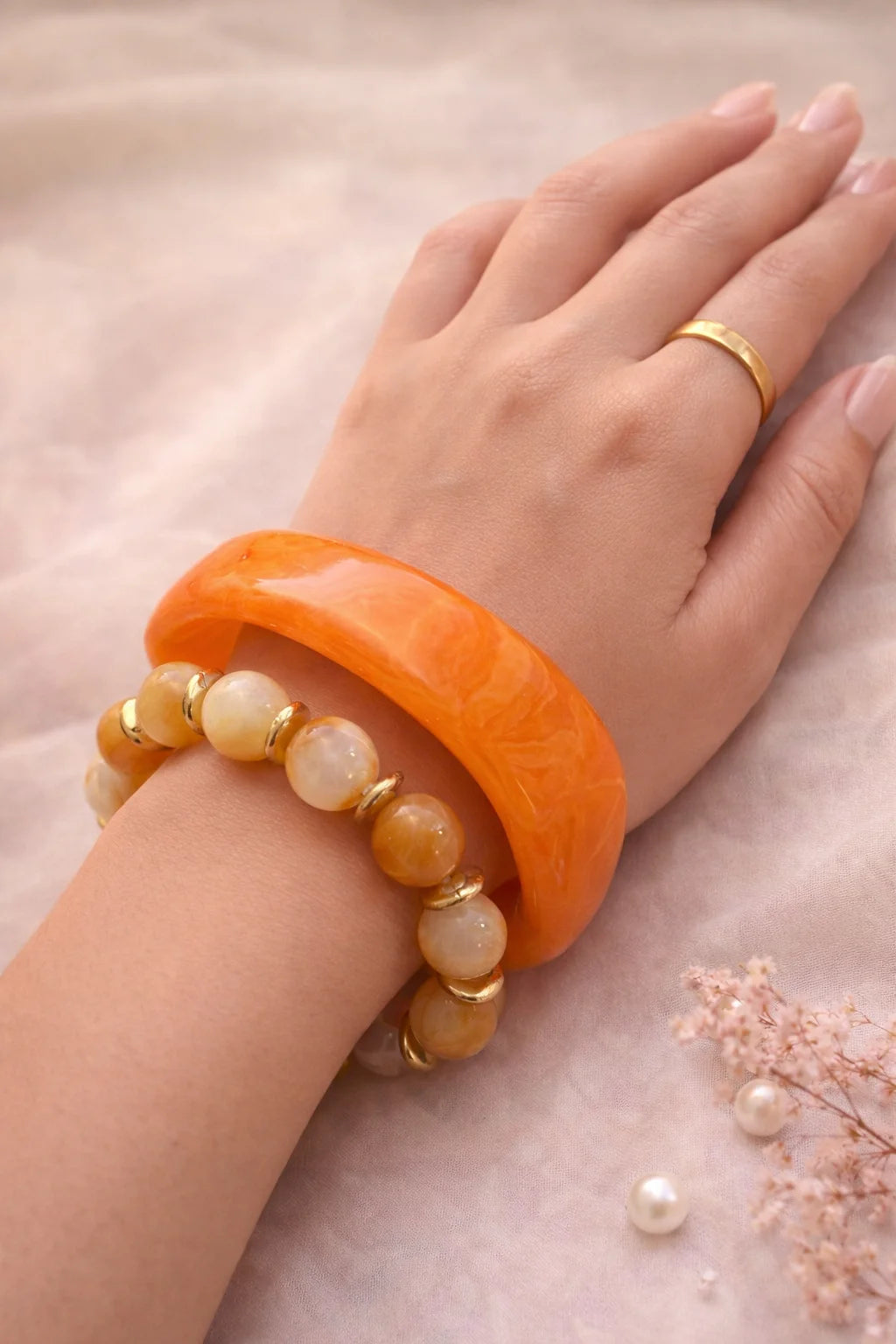 Orange resin bangle and beaded bracelet set with gold-tone ring on hand