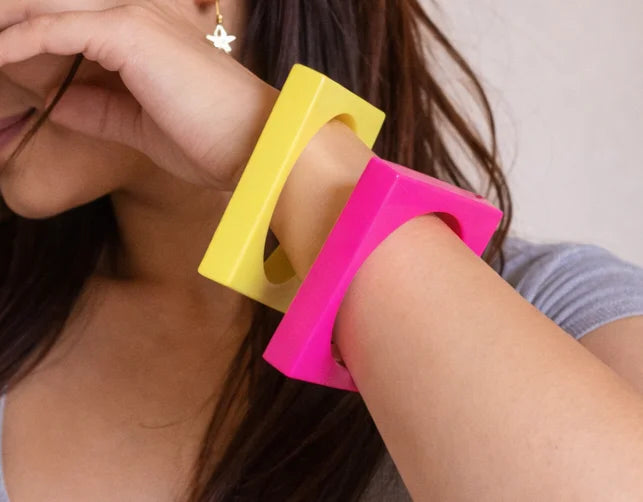 Wooden kada bangles in neon pink and yellow held in hand