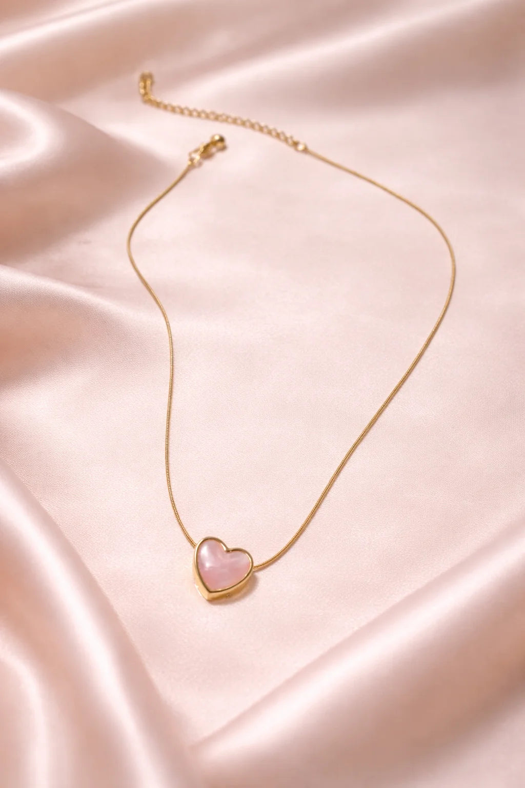 Gold necklace with blush-pink heart pendant on a slim chain.