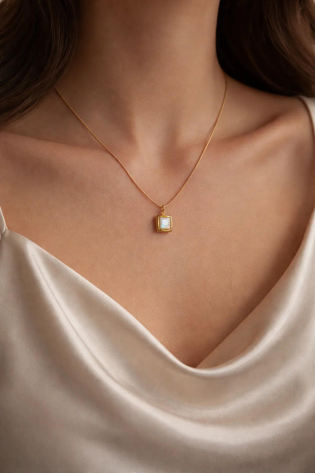 Gold-tone square pendant necklace with light stone on thin chain, worn at collarbone