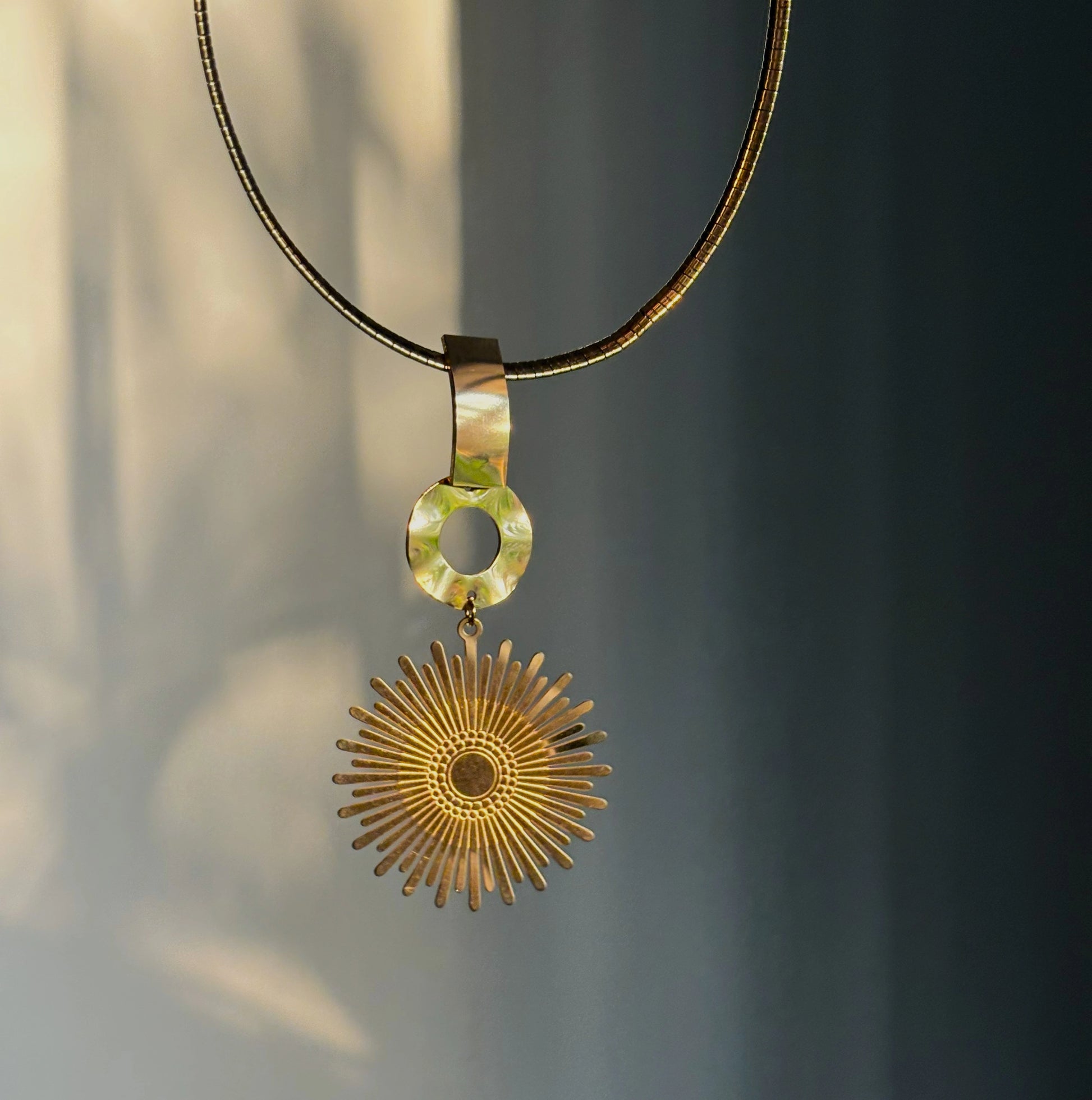 Gold choker necklace with reflective link and sunburst round charm pendant