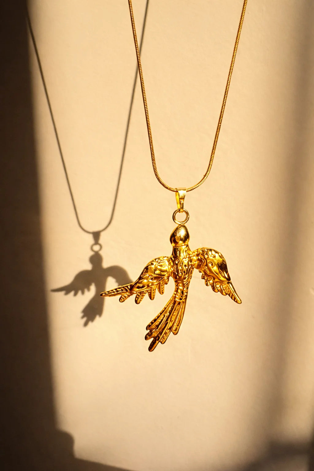 Gold bird pendant necklace with a long chain and detailed phoenix charm, gold clasp