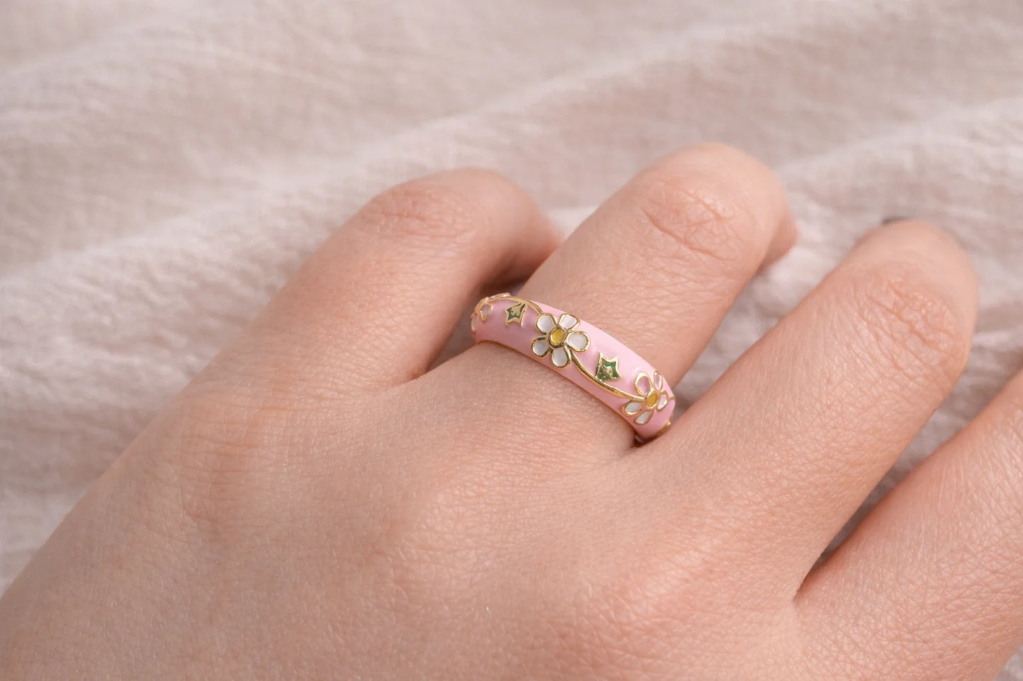 Pink enamel daisy ring on hand with gold-tone band and green leaf accents