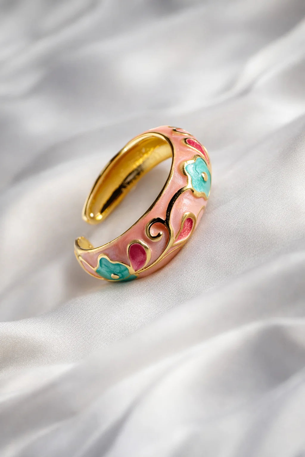 Gold-tone enamel ring band with pink scrollwork and teal floral insets, side view.