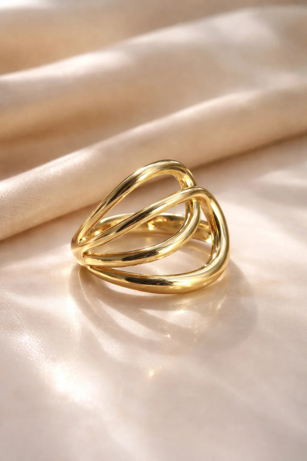 Gold-tone double-layer oval ring on satin fabric, interlocking loops with shine