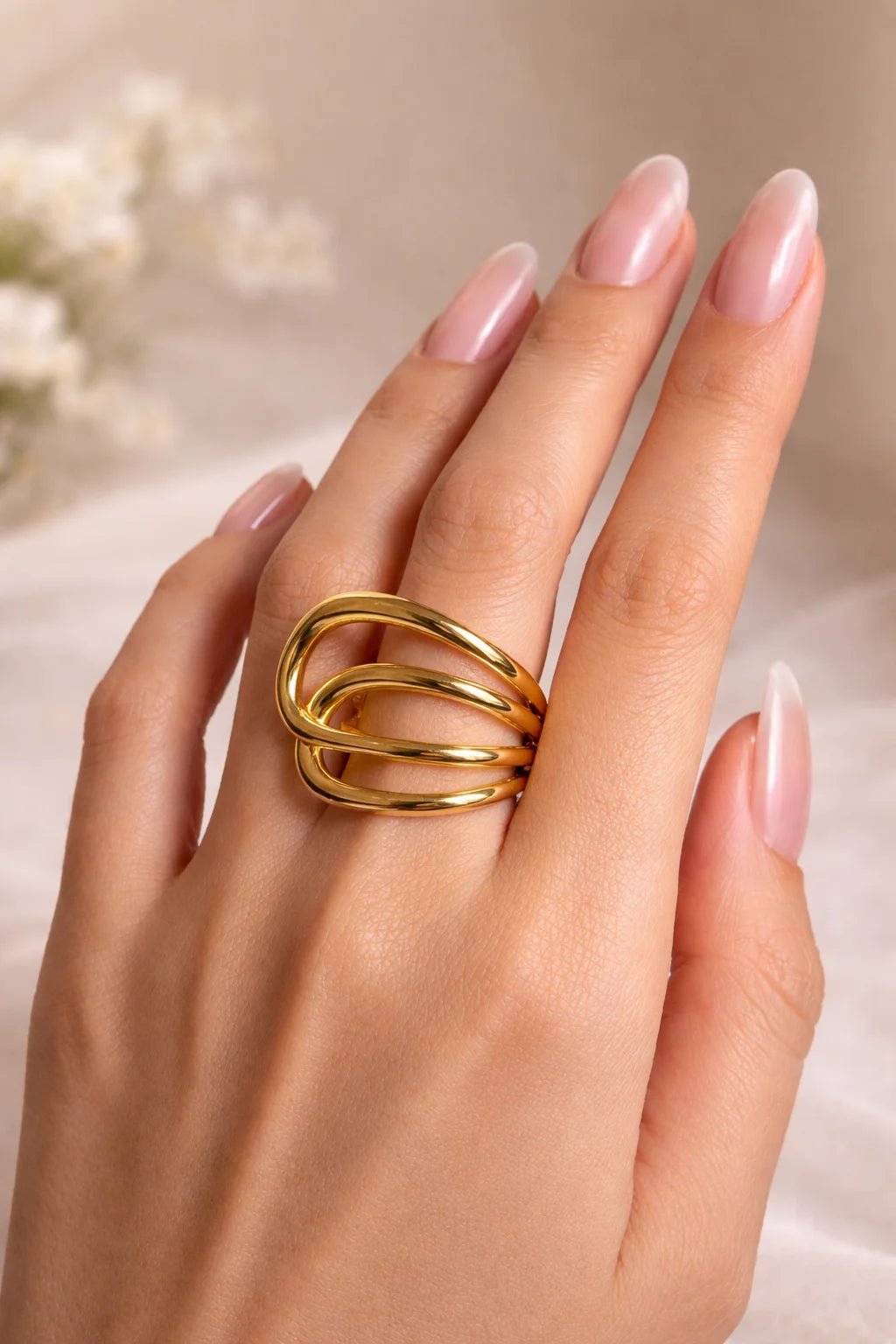 Gold-tone interlocking oval ring on finger with glossy double band and pink nails