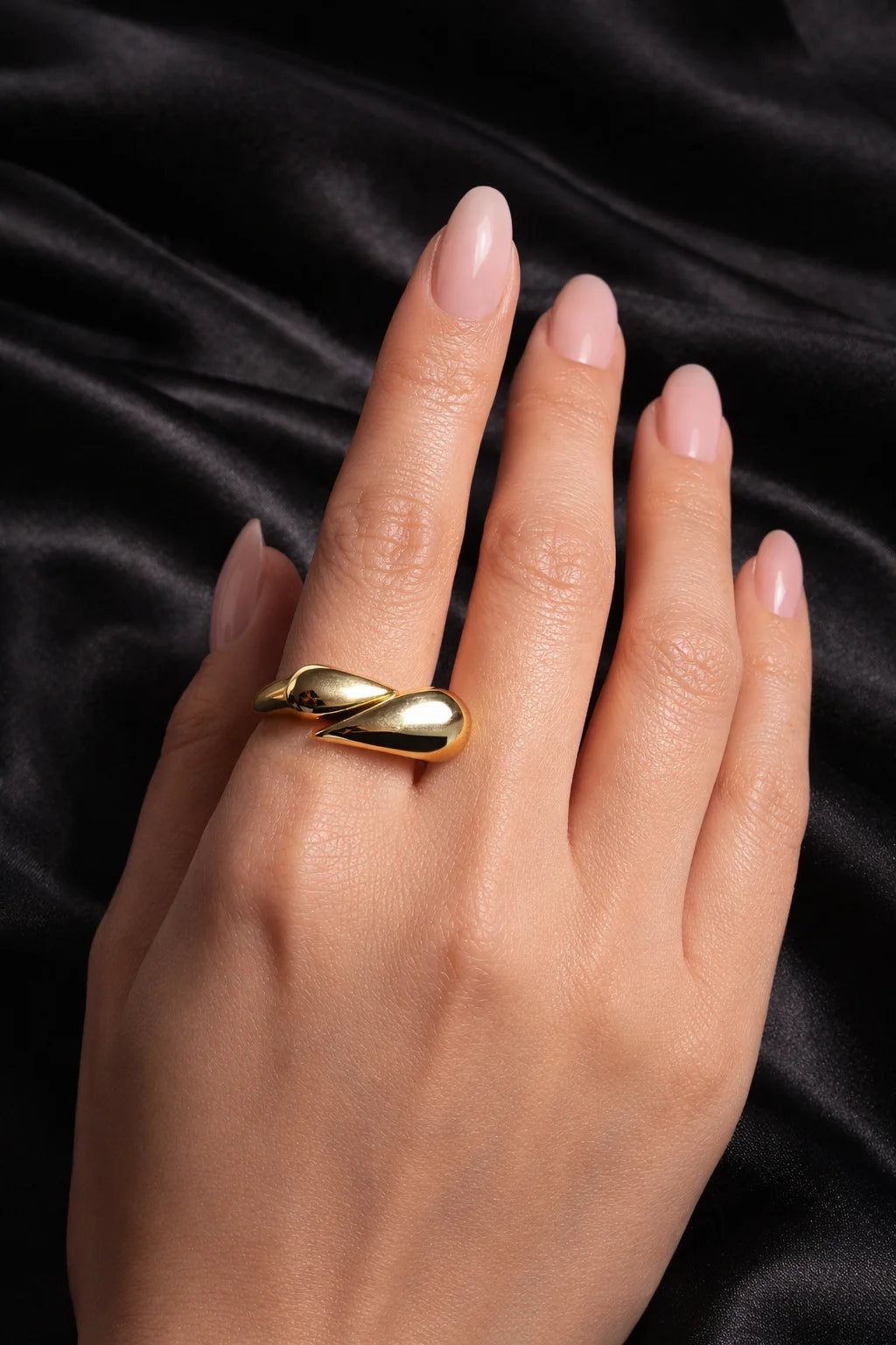Gold-tone teardrop hug ring on hand with glossy nude nails