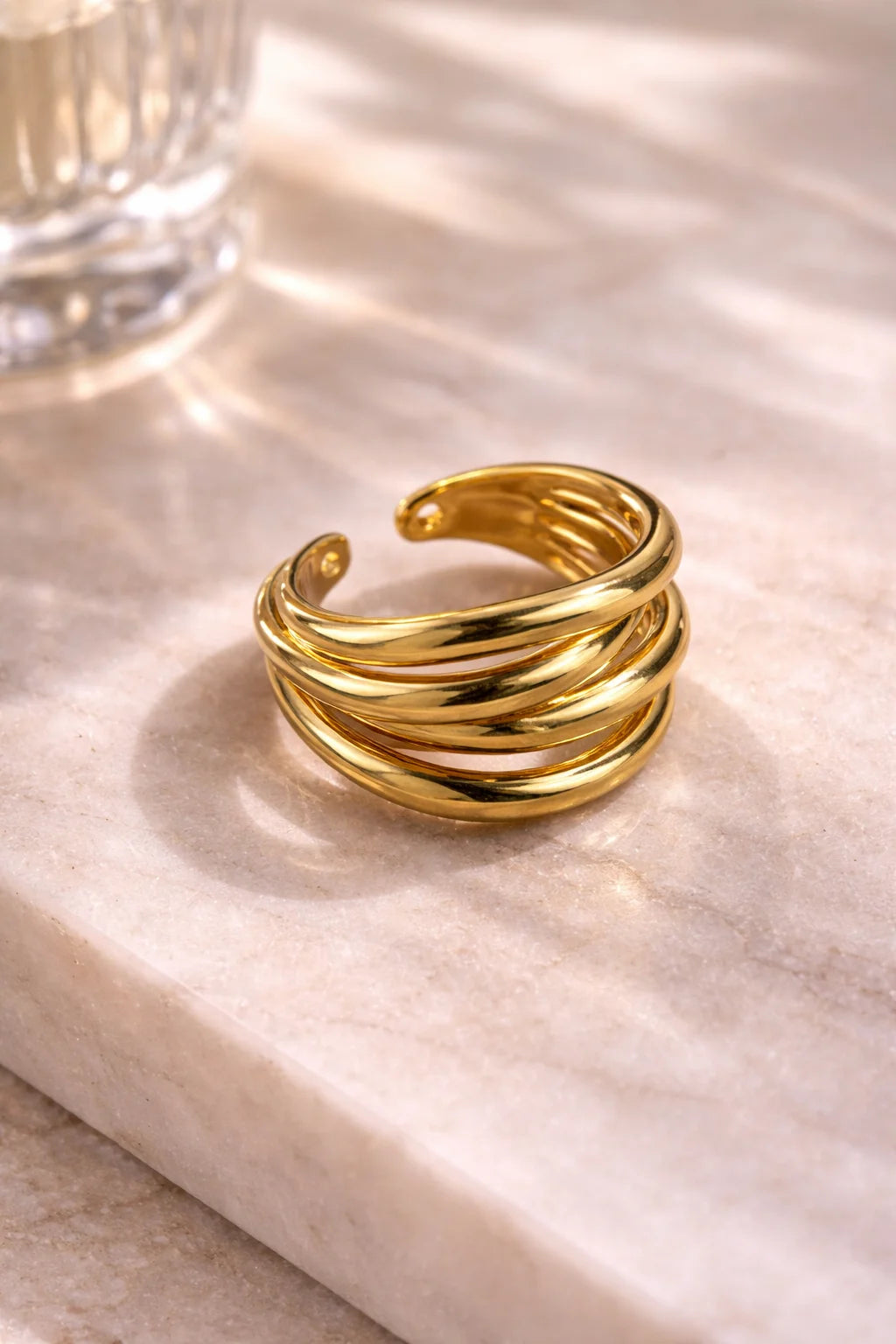 Gold four-layer spiral ring with layered bands on light stone base