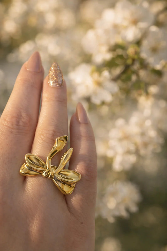 Gold-tone bow ring on finger, sculpted ribbon bow with dangling ends, open band
