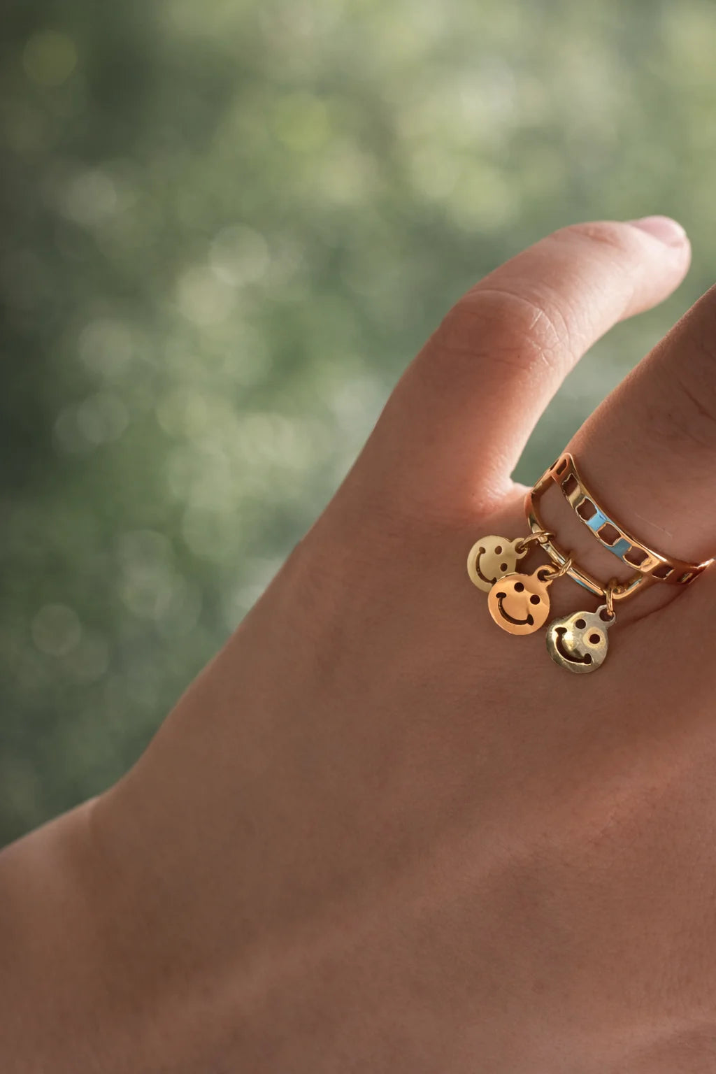 Gold-plated smiley charm ring with blue enamel square insets, worn on finger