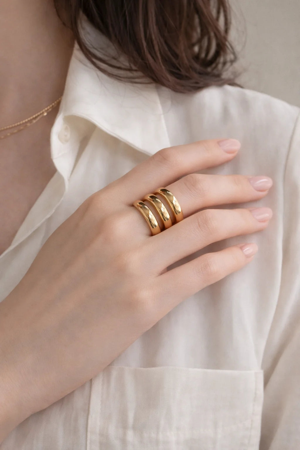 Gold three-layer ring on finger, stacked wide curved bands, polished
